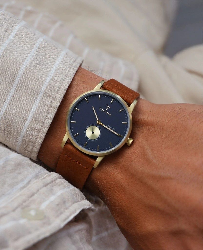 A Triwa Falken watch with a navy dial, gold case, and tan leather strap.